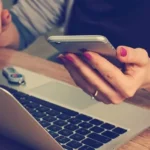 A person using a smartphone and laptop to access FINRA’s BrokerCheck tool