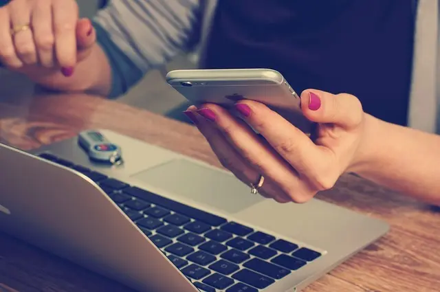 A person using a smartphone and laptop to access FINRA’s BrokerCheck tool
