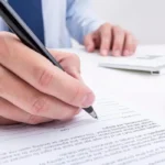 A person signing a line on a document using a pen.