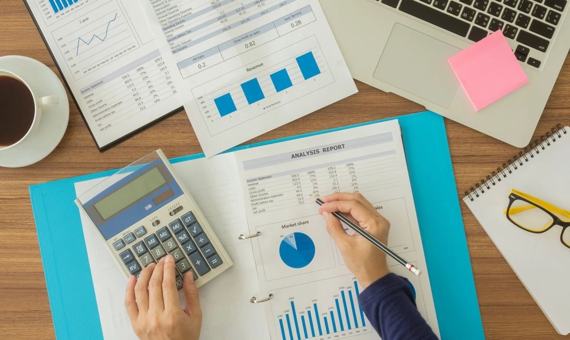 A person filling out an analysis report with one hand and typing it into a calculator with the other.