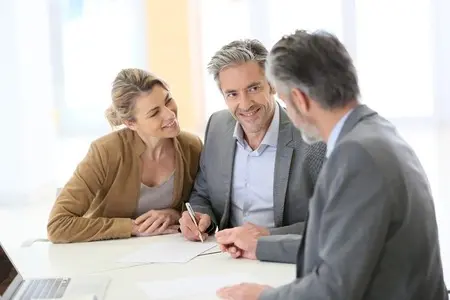 A husband and wife sign a document as another man looks on.