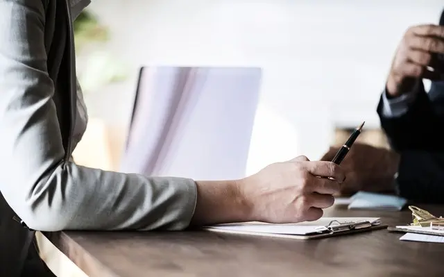 A person with an arm on a table holding a pen.