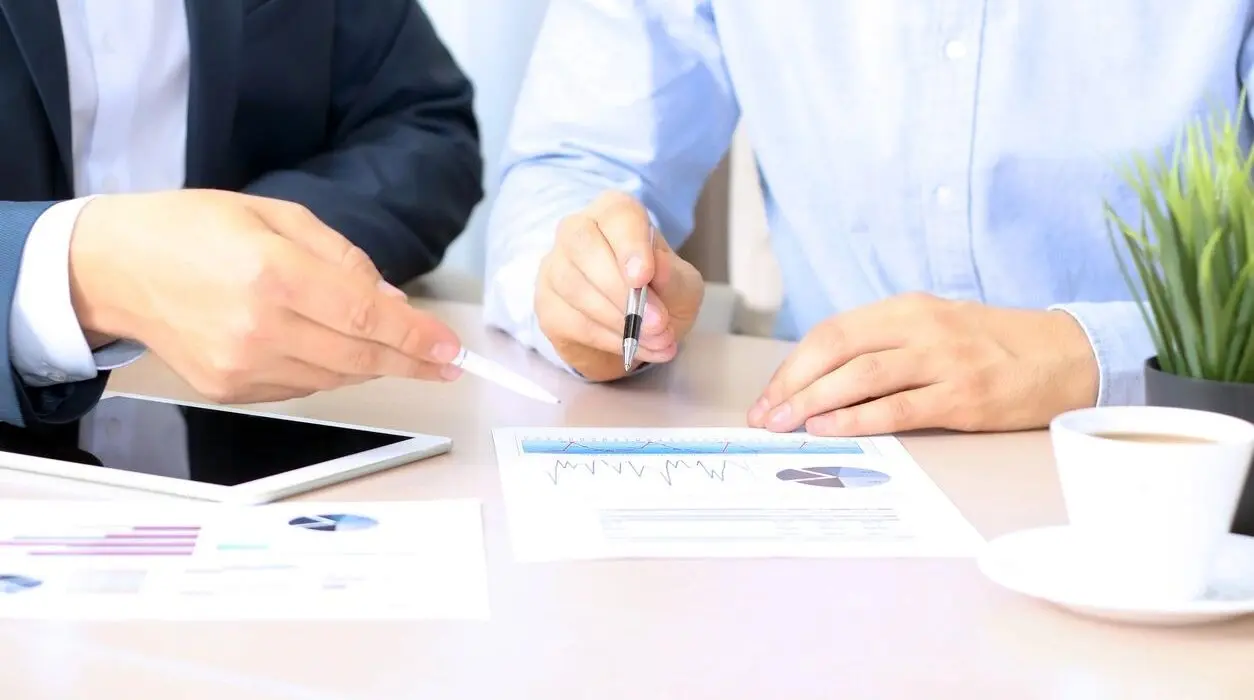 The hands of two people holding pens and pointing toward a paper with a financial report.