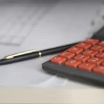 A pen and calculator next to forms from a company like Phoenix American Hospitality