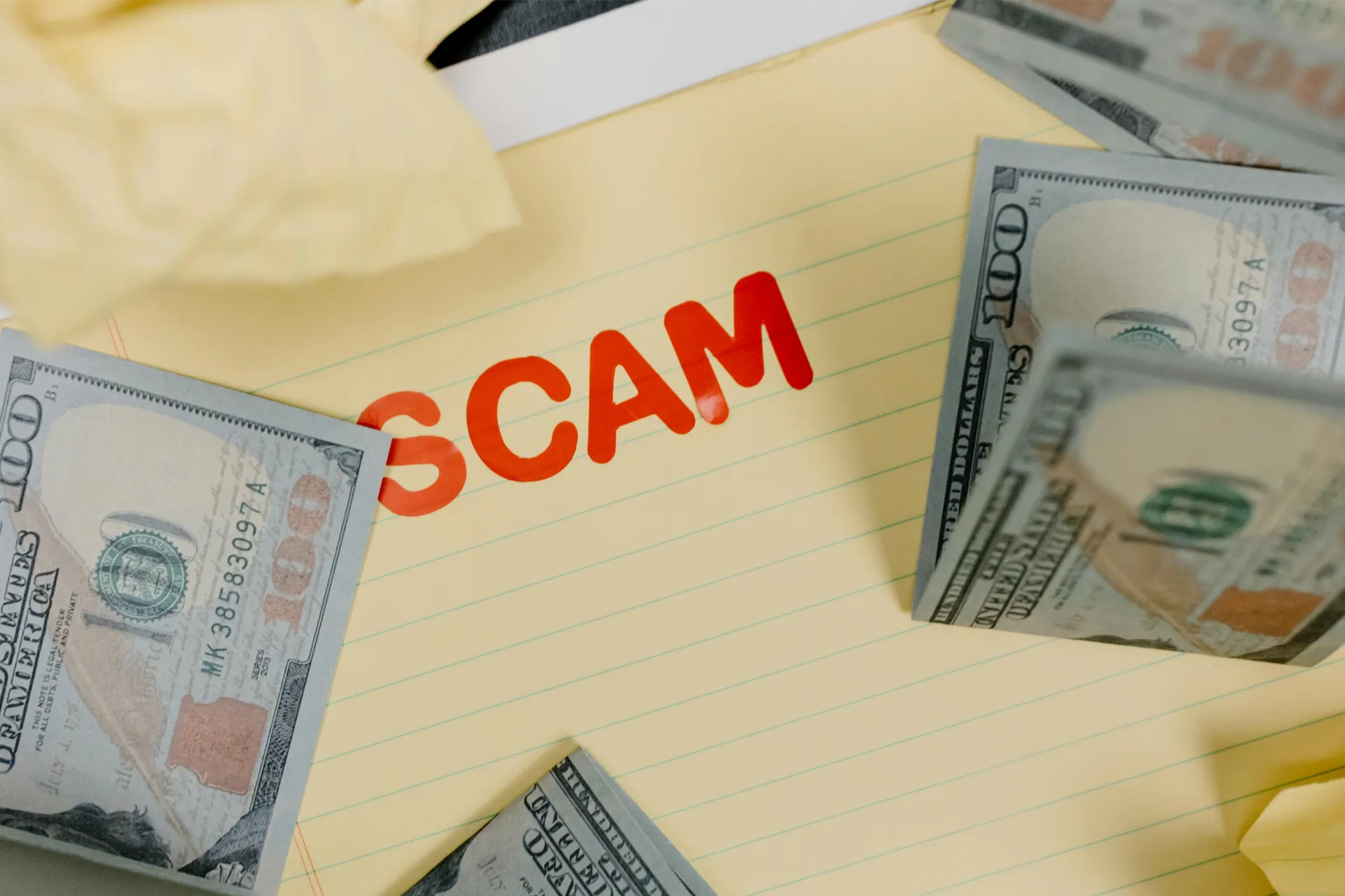 Several one-hundred-dollar bills following a notepad with the word “scam” on it