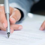 A person using a pen while looking over documents about Vincent Camarda